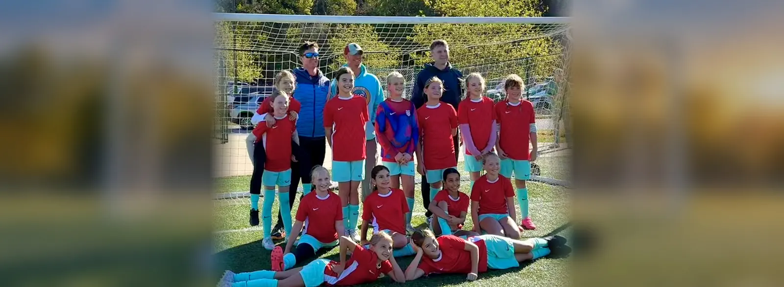 Junior Current soccer players and coaches posing together in front of a goal